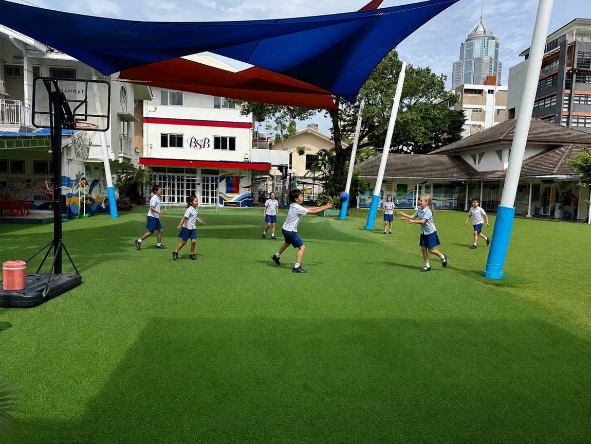 Students playing a ball game on the outdoor court with the Bangkok skyline behind the school